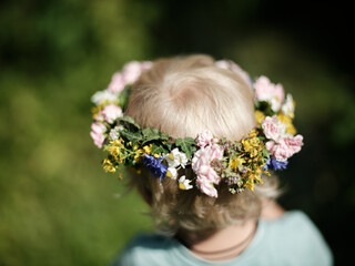 Blonde child with floral head wreath from behind