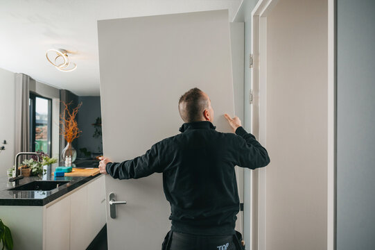 Carpenter installing white wooden door into doorframe