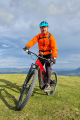 Obraz premium Cyclist man riding electric mountain bike outdoors. Male tourist biking along grassy trail in the mountains, wearing helmet and backpack. Concept of sport, active leisure and nature.