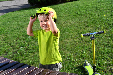 Cute little boy putting on a safety helmet before riding a scooter.