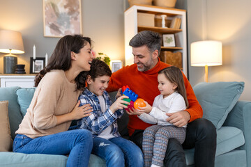 Cheerful son and daughter sitting with parents playing at home. Playful little boy and girl enjoying spending time with parents at home.