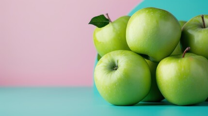 A stacked bunch of glossy green apples with a single leaf on top, arranged artistically against a pink and teal abstract background for a pleasant visual effect.