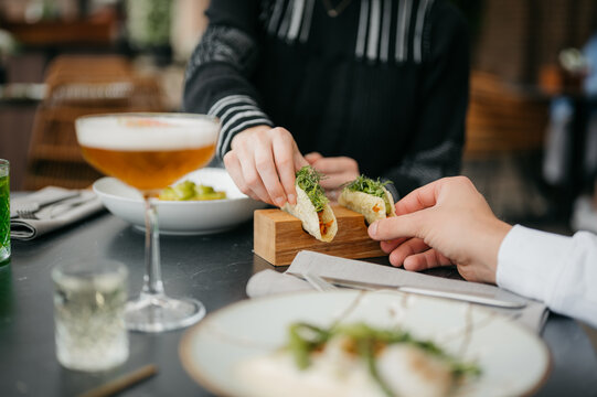 Person grabbing a fancy taco from a wooden plate in a fancy restaurant