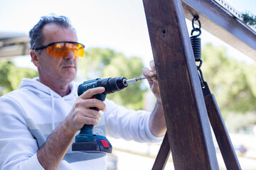 Man in protective eyewear using power drill outdoors