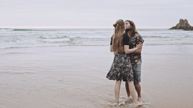 Joyful Gen Z couple enjoys fun summer evening at the beach, running, walking on sand in the ocean. Embracing love, happiness, smile, savor vacation together on the coast, creating lasting memories.