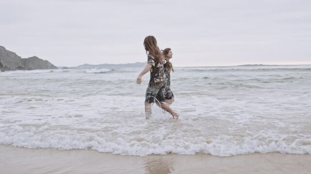 Joyful Gen Z couple enjoys fun summer evening at the beach, running, walking on sand in the ocean. Embracing love, happiness, smile, savor vacation together on the coast, creating lasting memories.