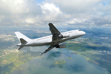 White airplane flying in the sky among white dense clouds floating over land surface. Colorful travel background