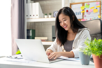 Beautiful young Asian woman student studying online with laptop computer at home.