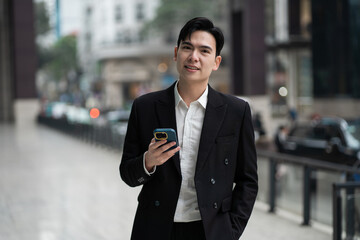 Portrait of a young Asian business man on the street with tall buildings behind him