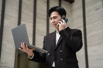 Portrait of a young Asian business man on the street with tall buildings behind him