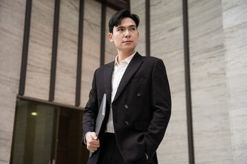 Portrait of a young Asian business man on the street with tall buildings behind him