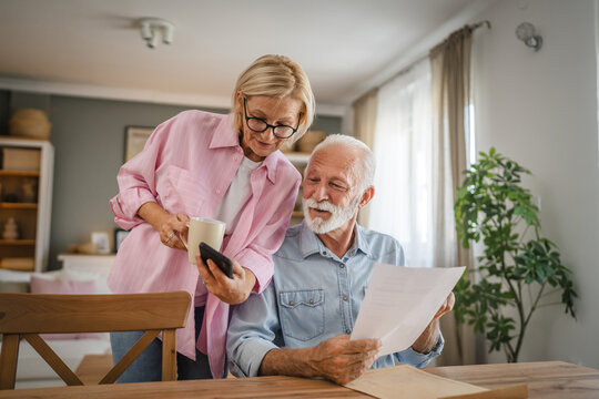senior couple read a document from envelope and use cellphone together