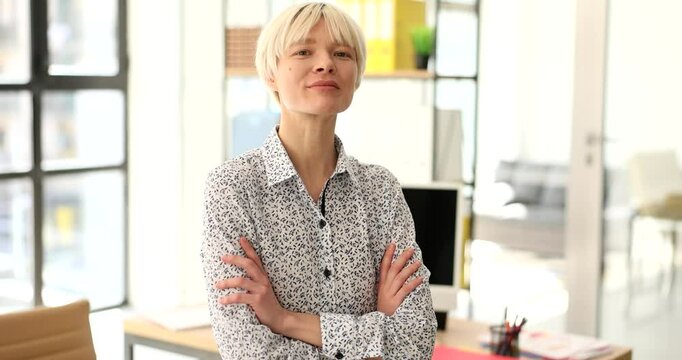 Confident blonde woman crosses arms posing for camera in office slow motion. Drastic young female entrepreneur at workplace. Business start strategy