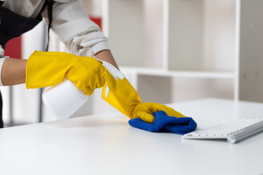 Young Asian cleaning woman uses a cloth to wipe clean a computer and keyboard using cleaning solution in her home office.