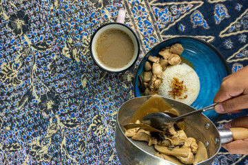 hand pouring a gravy in the rice plate with coffee on the background