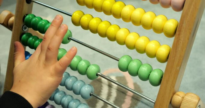 Little boy hand moves green balls on abacus counting in daycare classroom closeup. Toddler student learns to add numbers with colorful wooden toy
