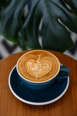 Latte art on wooden table with monstera leaf