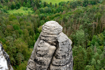 A large rock formation with a green forest in the background. The rock is shaped like a human...