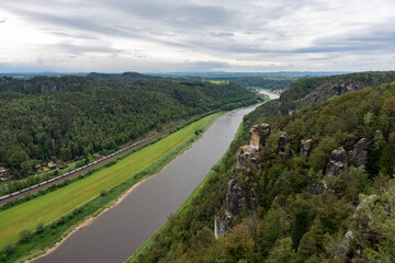 A river runs through a lush green valley. The sky is cloudy, and the trees are tall and green