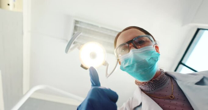 POV, dentist and thumbs up in surgery for success, consultation and approval by light. Female specialist, mask and yes in clinic for dental care, insurance and hand gesture for happy with results