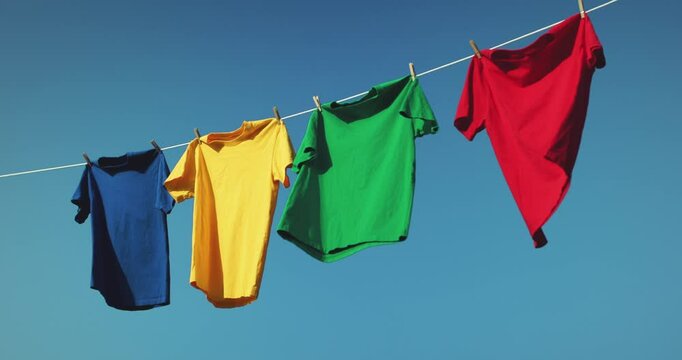 Colorful t-shirts drying on washing line against blue sky
