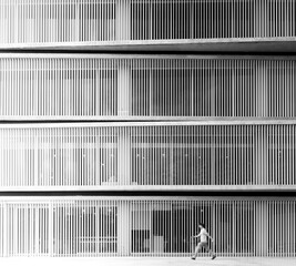 The white gradient vertical steel stripes exterior wall of a building with a man walking passed, black and white monotone. 