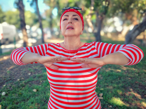 Determined cancer fighter: woman performs breathing exercises in park, embracing active lifestyle despite chemotherapy.