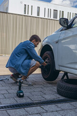 Young man in unscrewing lug nuts on car wheel in process of new tire replacement,using wrench while changing flat tire on the road.