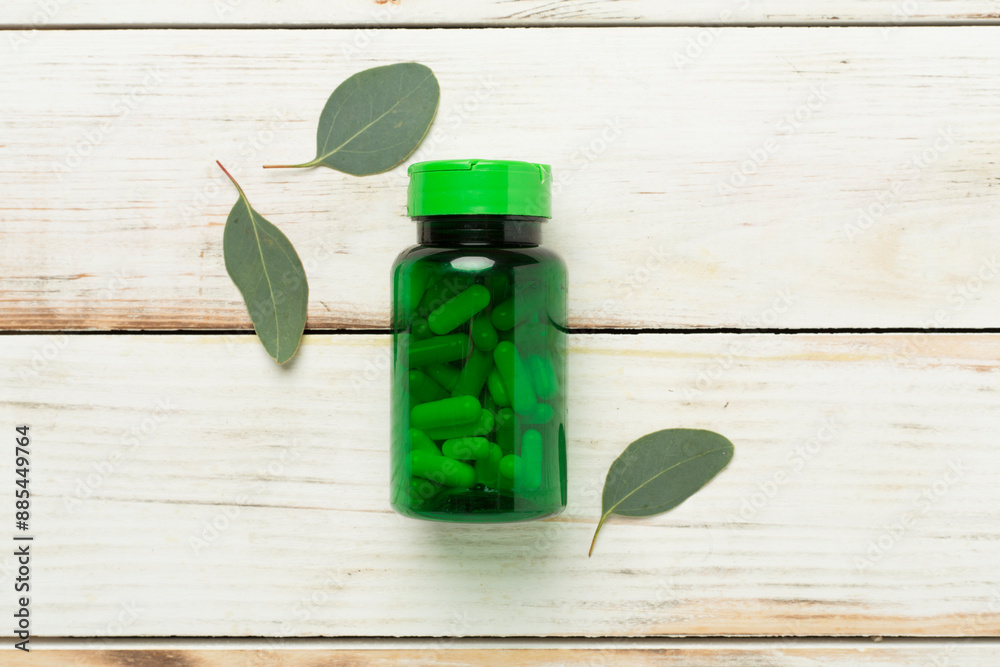 Sticker Bottle with pills and green leaves on wooden background, top view