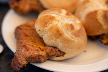 A piece of meat is on a white plate with a bun on top of it. The bun is slightly burnt, giving the dish a rustic and hearty appearance. The meat is likely a pork chop