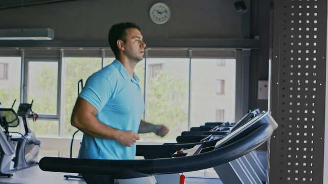 Cardio workout. Active guy exercising on treadmill at gym, side view, slow motion