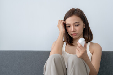 Woman looking at pill bottle with concern while sitting on a couch. Concept of health, medication,...