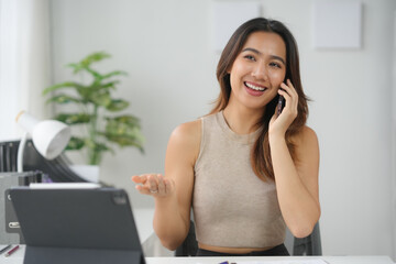 Smiling woman talking on phone at desk with laptop, enjoying a pleasant conversation in a modern...