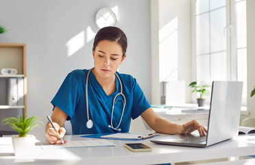 Young busy female nurse is concentrating on working while sitting at desk at workplace in clinic....