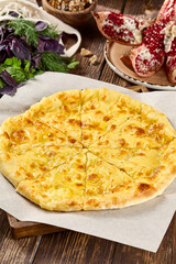Traditional Ossetian Cheese Pie on Rustic Wooden Table with Fresh Herbs and Pomegranate