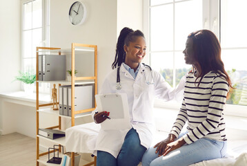 Obraz premium Happy smiling woman patient talking with friendly african american female doctor therapist holding report file with appointment sitting on the couch in office during medical examination in clinic.