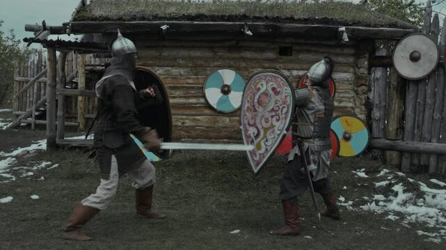Full slowmo shot of two medieval knights practicing sword-fighting skills together in fortress yard, hacking at each others shields, dodging blows, while getting ready for combat in wartime