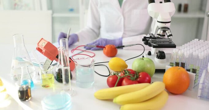Female scientist checks nitrate content in fresh fruits and vegetables using laboratory equipment. Woman writes down results of examination slow motion