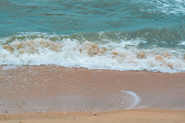View of blue sea waves and white foam on a sand beach at Pattaya City Resort in Thailand.
