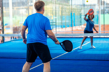 Mixed adult couple playing padel on outdoor court.