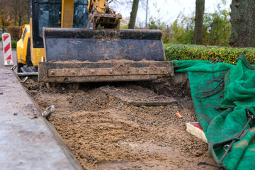 Konzept Baustelle: Frontalansicht aus der Froschperspektive auf einen Schaufelbagger an einer Straße mit Warnbarke und viel Copy Space im Vordergrund, selektiver Fokus