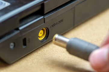 Man's hand plugging in connecting a power supply adapter cord plug into a generic laptop computer...