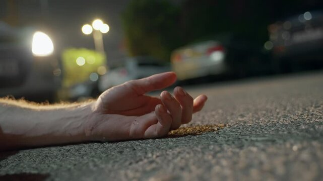 Man's hand lies motionless, illuminated by the flashing lights of a police car. Tragic scene on a dark road. Potential crime scene, Murder case. dead guy on the ground. police crime scene. being shot.