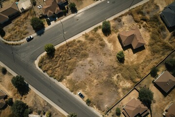 Aerial view of suburban street and empty lot bordered by houses and trees