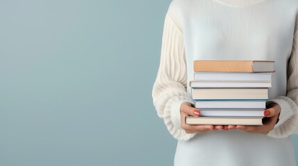 Person holding a stack of books against a light blue background, wearing a white sweater. Concept of reading, education, or knowledge.