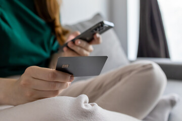 The girl is using a credit card. The girl is sitting on the couch.