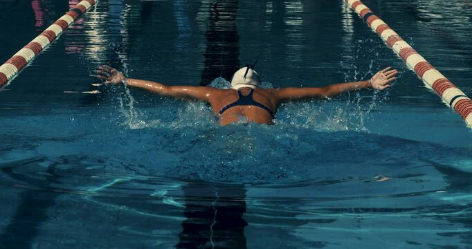 Super slow motion of young professional female swimmer with cap and goggles swimming with passion and motivation to achieve a victory in competition while practicing in swimming pool.