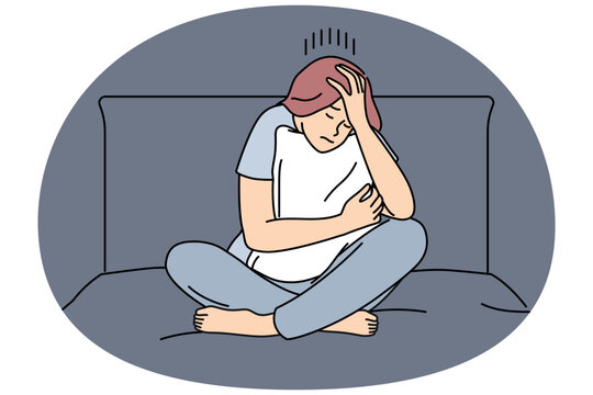 Melancholic woman is sad sitting on bed and hugging pillow after quarrel with boyfriend or divorce from husband. Melancholic girl suffers from headache causing insomnia and chronic fatigue.
