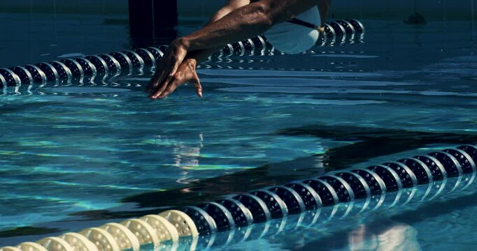 Super slow motion of young professional male swimmer with cap and goggles swimming with passion and motivation to achieve a victory in competition while practicing in swimming pool.