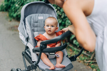 Portrait of a baby sitting in a stroller with her mother leaning towards her during a walk.